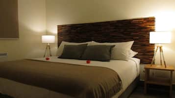 A hotel room with a bed, two bedside lamps, a wooden headboard, and a window with blinds.