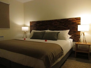 A hotel room with a bed, two bedside lamps, a wooden headboard, and a window with blinds. - Parador Loberias del Sur Puerto Bertrand (Chile Chico)
