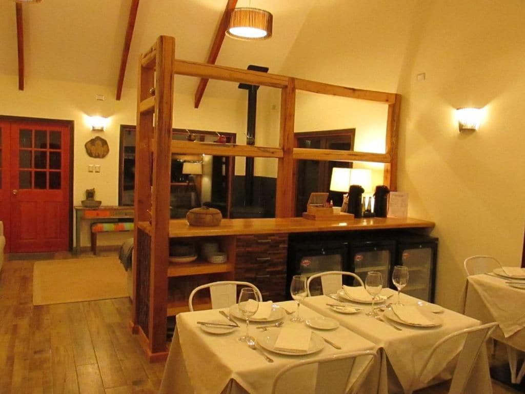 A dining area with tables set for four, wooden beams, and a kitchen visible in the background.