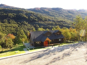 A two-story log cabin with a red door, surrounded by a gravel driveway and a well-maintained lawn. - Parador Loberias del Sur Puerto Bertrand (Chile Chico)