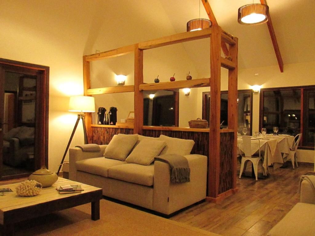 A living room with a sofa, a coffee table, a dining area with a table and chairs, and a wooden partition with shelves.