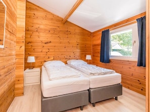 A wooden cabin room with a bed, a nightstand, and a window with curtains. - Holiday Home in Renesse With Swimming Pool (Renesse)