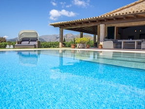 A clear swimming pool with a patio area, outdoor furniture, and a view of mountains in the background. - Villa Seguinot Gran (Pollença)