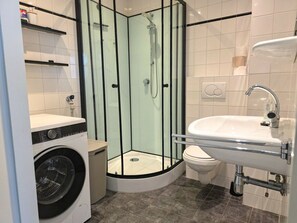 A compact bathroom with a glass-enclosed shower, a washing machine, a toilet, and a sink. - We09 Holiday Home for 6 People (Westkapelle)