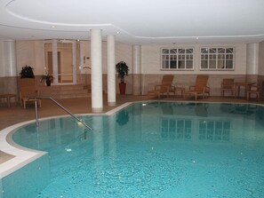 An indoor swimming pool with a clear water surface, surrounded by lounge chairs and potted plants. - 7 Residence Bismarck (Sylt)