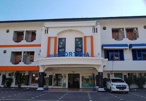 Un hotel llamado 'HOTEL FOR TUNA' con una entrada destacada, un área de estacionamiento y fachada de edificio blanca.