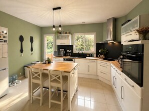 A modern kitchen with white cabinetry, a wooden island, and a black stove. - Villa on the ramparts with a terrace and a view of the Pyrenees (Montaut)