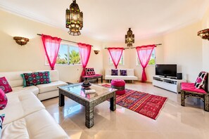 Ein modernes Wohnzimmer mit Sofa, Couchtisch und Fernseher, ausgestattet mit dekorativen Kissen und einem gemusterten Teppich.