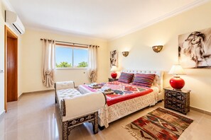 Un dormitorio con cama, mesita de noche, lámpara, alfombra y ventana con cortinas.