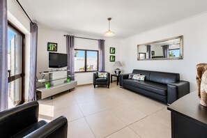 A modern living room with a flat-screen TV, a sofa, a coffee table, and a dining area with a glass top. - Villa Lela - Two Bedroom Villa, Sleeps 4 (Vale Rebelho)