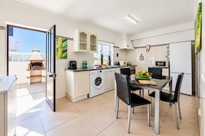 A modern kitchen with a built-in oven, washing machine, and dining area with chairs and a table. - Villa Lela - Two Bedroom Villa, Sleeps 4 (Vale Rebelho)