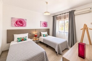 Una habitación de hotel con dos camas, una mesita de noche con una lámpara, un cuadro y un caballete de madera.