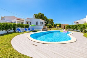 A swimming pool with a curved edge, surrounded by a paved deck and a grassy area. - Villa Rosa dos Ventos (Vale Rebelho)