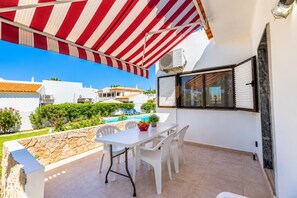 A balcony with a table and chairs, a pool in the background, and a view of neighboring houses. - Villa Rosa dos Ventos (Vale Rebelho)