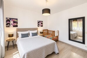 A bedroom with a bed, a crib, a mirror, and artwork on the walls. - Villa Rosa dos Ventos (Vale Rebelho)
