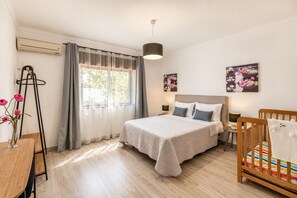 Quarto com cama, mesas de cabeceira, berço, janela com cortinas e um quadro na parede.