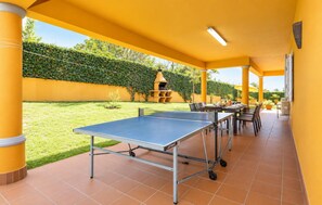 Ein Außenbereich mit Tischtennisplatte, Stühlen und einem Esstisch mit Sonnenschirmen.