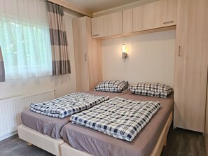 A bedroom with a bed, two bedside tables, a window with curtains, and a wall-mounted light. - Ok31 Family Chalet (Oostkapelle)