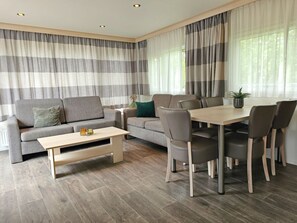 A modern living room with a sofa, coffee table, and dining area with chairs. - Ok31 Family Chalet (Oostkapelle)