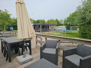 An outdoor patio area with wicker furniture and a table, a covered umbrella, and a soccer goal in the background. - Ok31 Family Chalet (Oostkapelle)