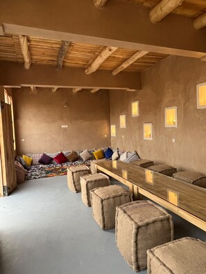 A room with a long wooden table, several cushioned seating options, and a rustic ceiling. - Zaim Heritage Kasbah (Skoura)