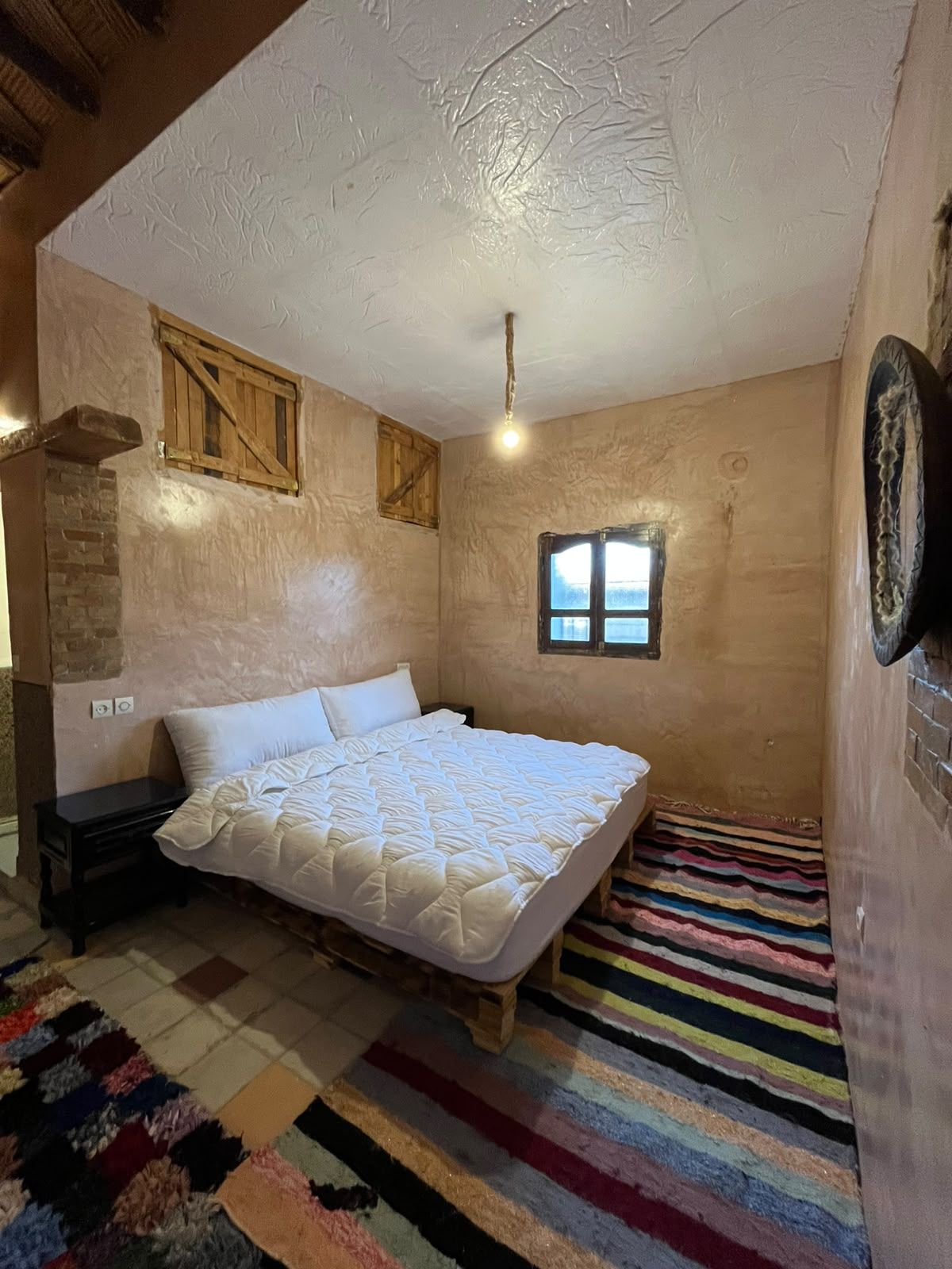 A bedroom with a bed, a nightstand, a window, and a wooden wall.