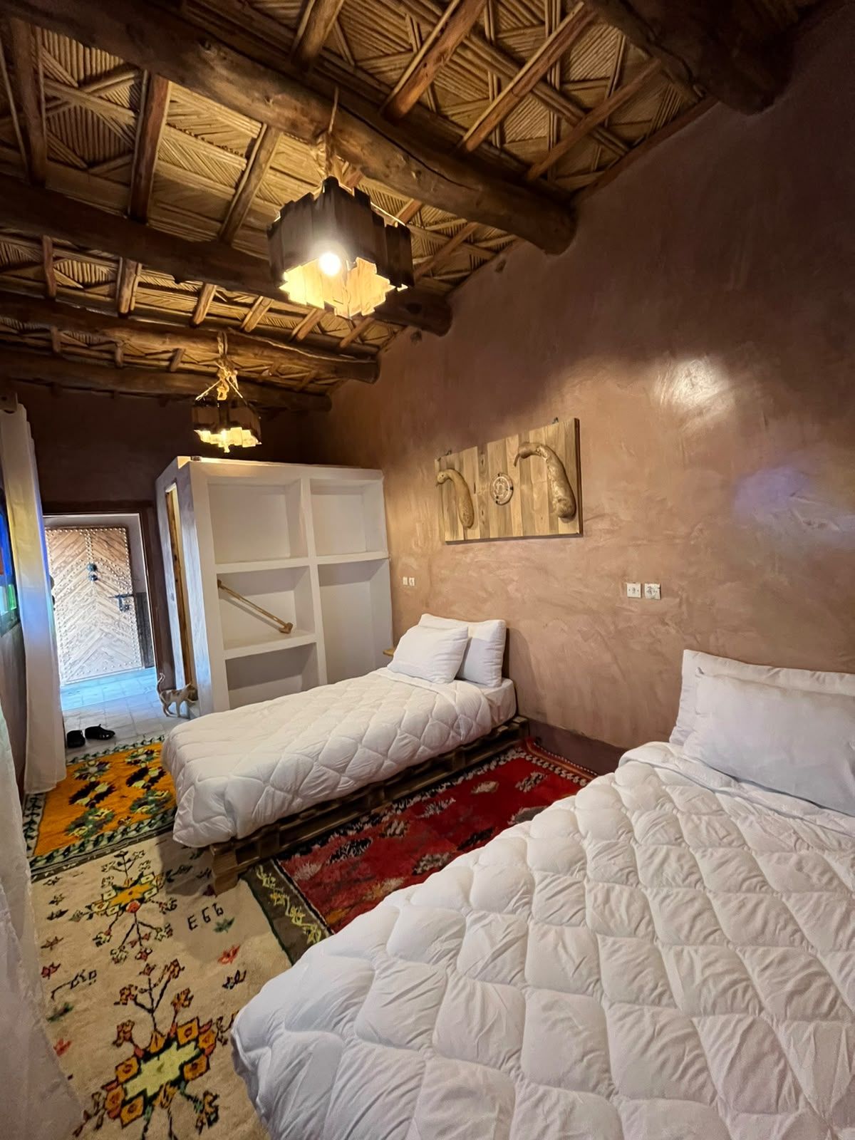 Une chambre avec deux lits, un plafond en bois, un luminaire suspendu et un tapis à motifs.