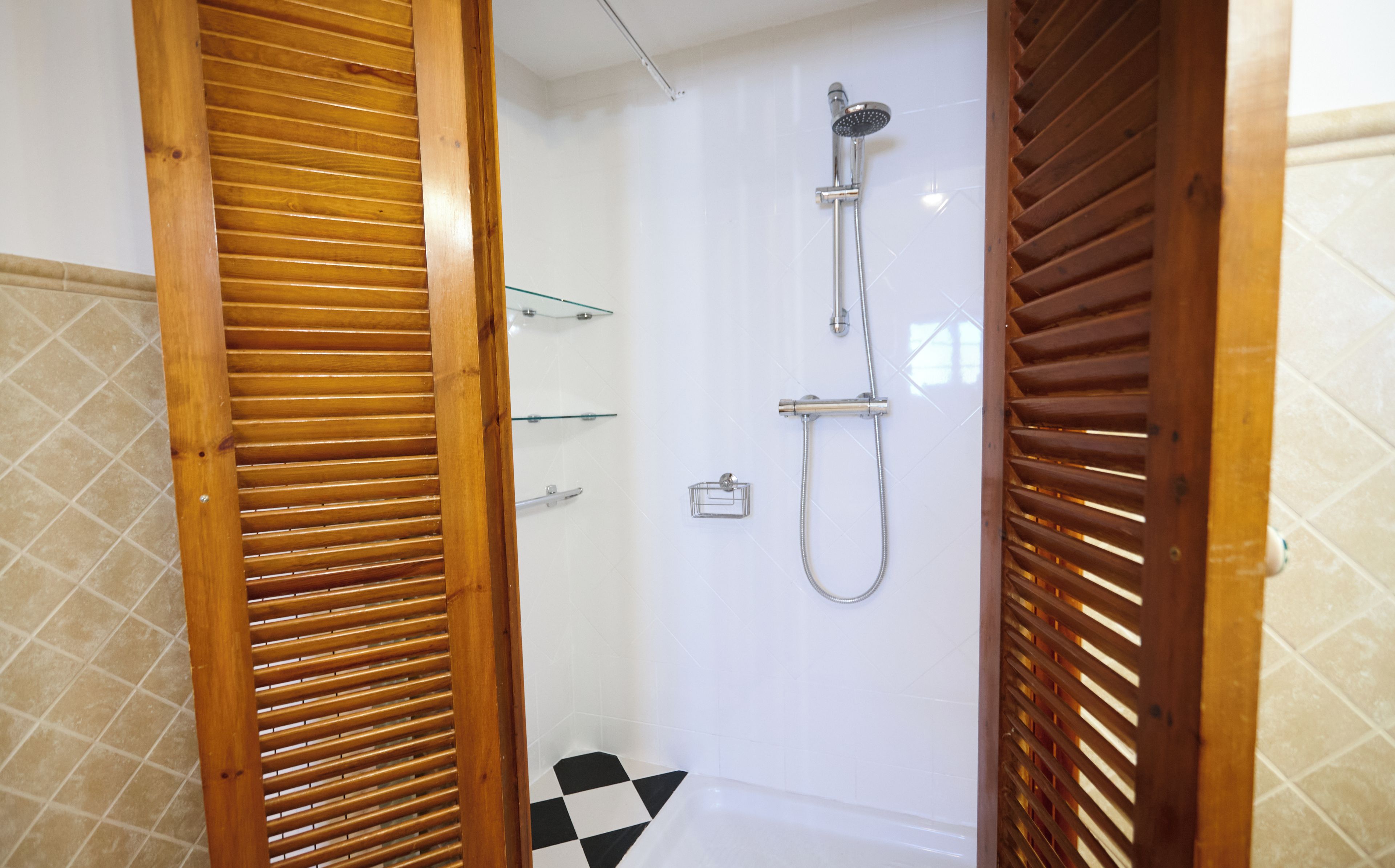 Un baño con ducha, estante de vidrio y piso a cuadros.
