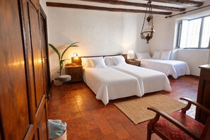 A hotel room with two beds, a wooden floor, a large window, and a hanging light fixture.