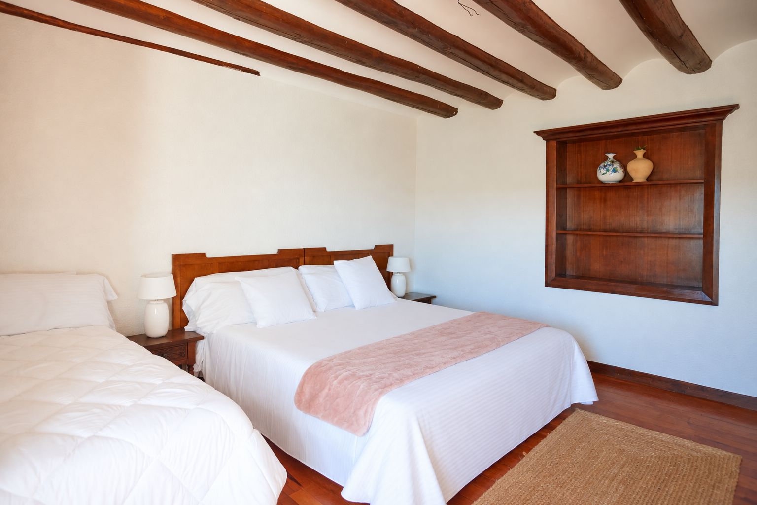 Un dormitorio con una cama doble, una mesita de noche, una lámpara de noche y un estante de madera con objetos decorativos.