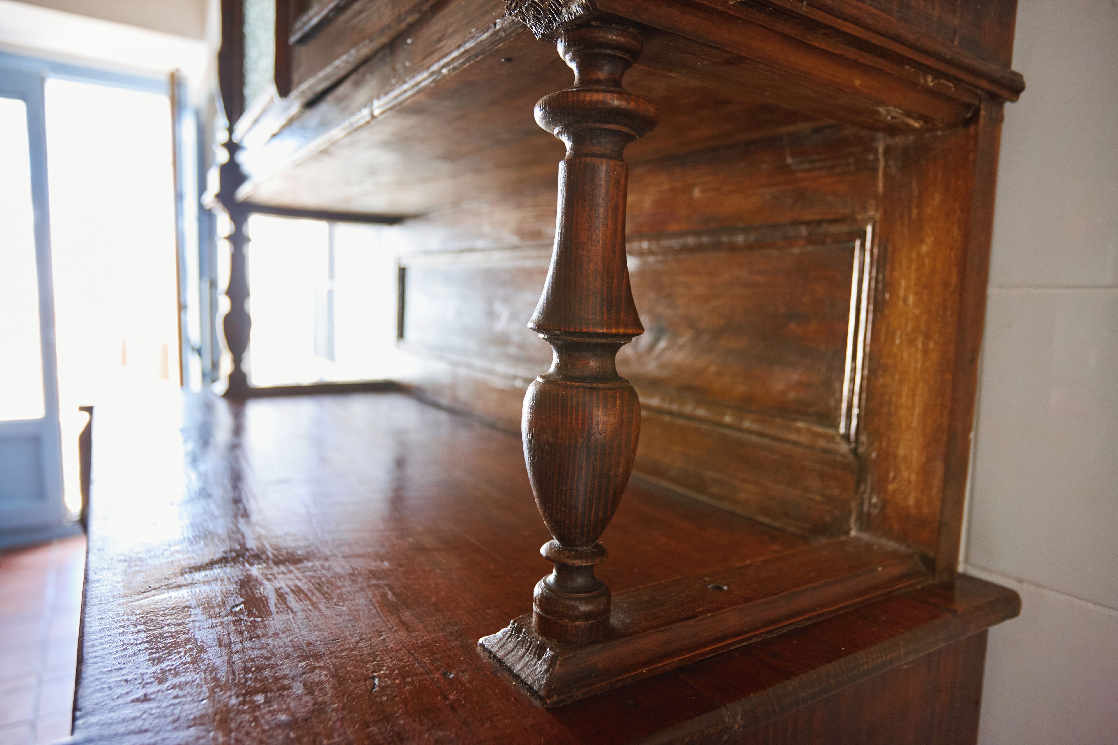A wooden table with a carved leg, part of a room with a wooden wall and a door in the background.