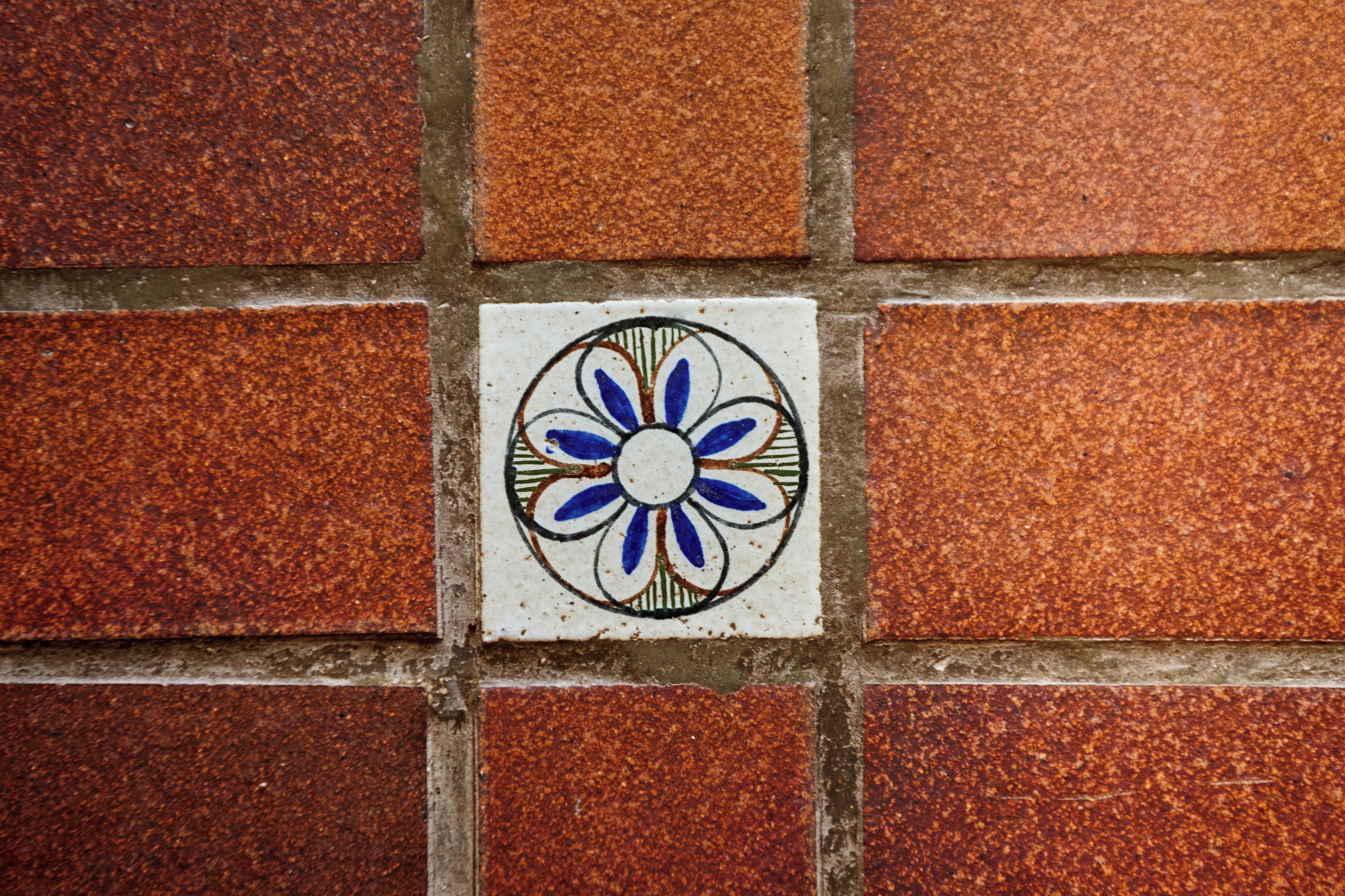 Un mur recouvert de carreaux, avec un seul carreau décoratif présentant un motif floral bleu et blanc.