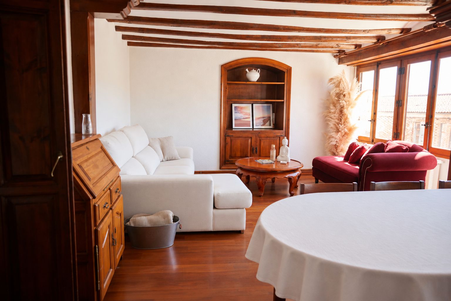 Un salon chaleureux avec un canapé blanc, un fauteuil rouge, un meuble en bois et une table ronde.
