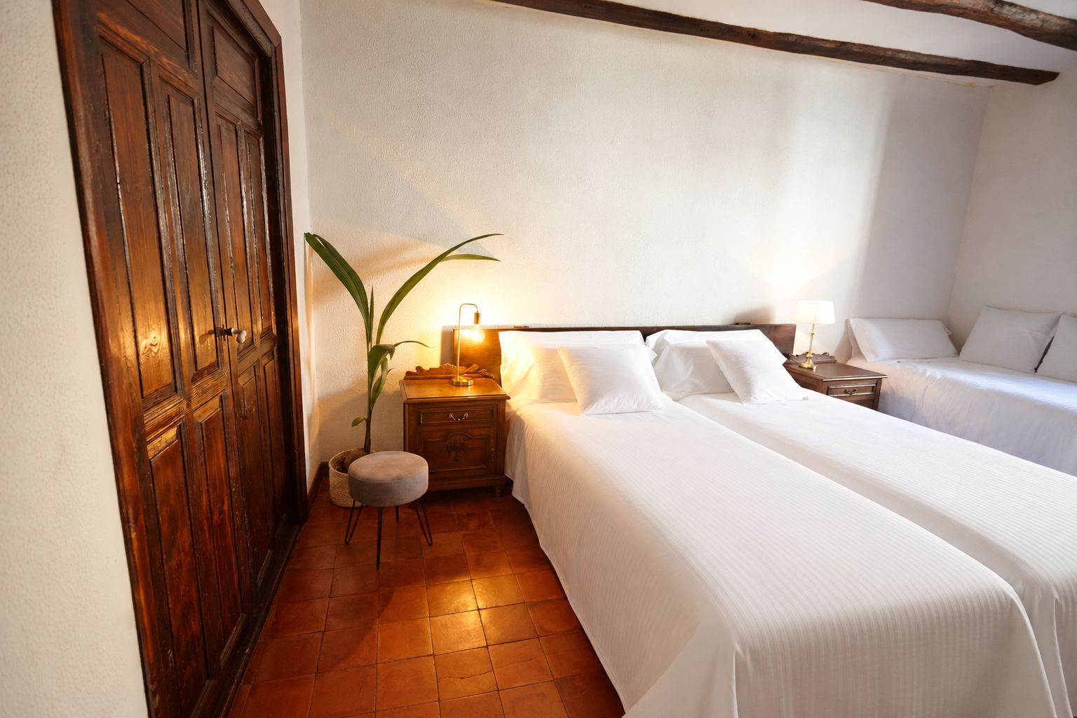 Habitación de hotel con dos camas, un armario de madera, una mesita de noche con lámpara y una planta en maceta.