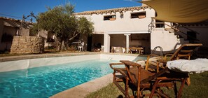 A swimming pool with lounge chairs, a stone wall, and a building with a tiled roof.
