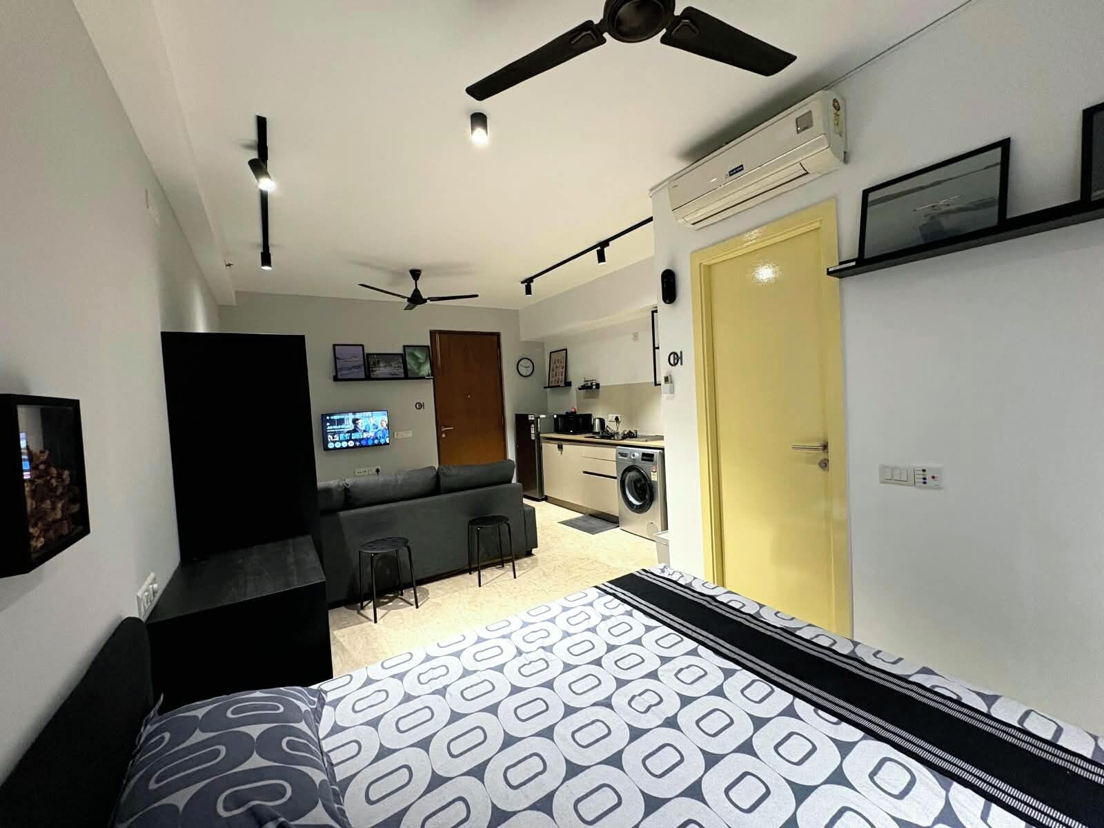 A compact living space with a bed, a sofa, a small kitchen area, and a ceiling fan.