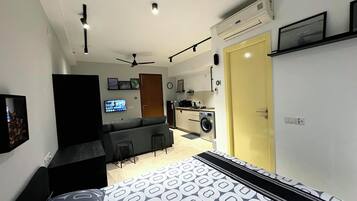 A compact living space with a bed, a sofa, a small kitchen area, and a ceiling fan.
