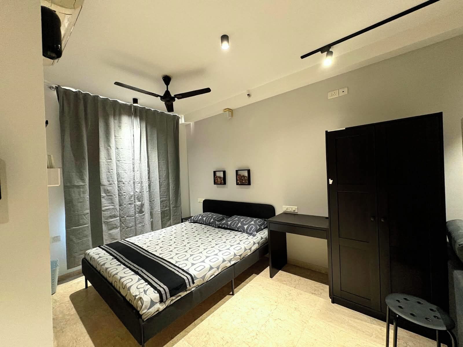 A bedroom with a bed, a desk, a wardrobe, and a ceiling fan.