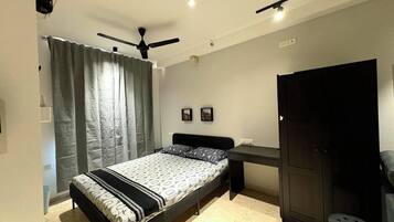 A bedroom with a bed, a desk, a wardrobe, and a ceiling fan.