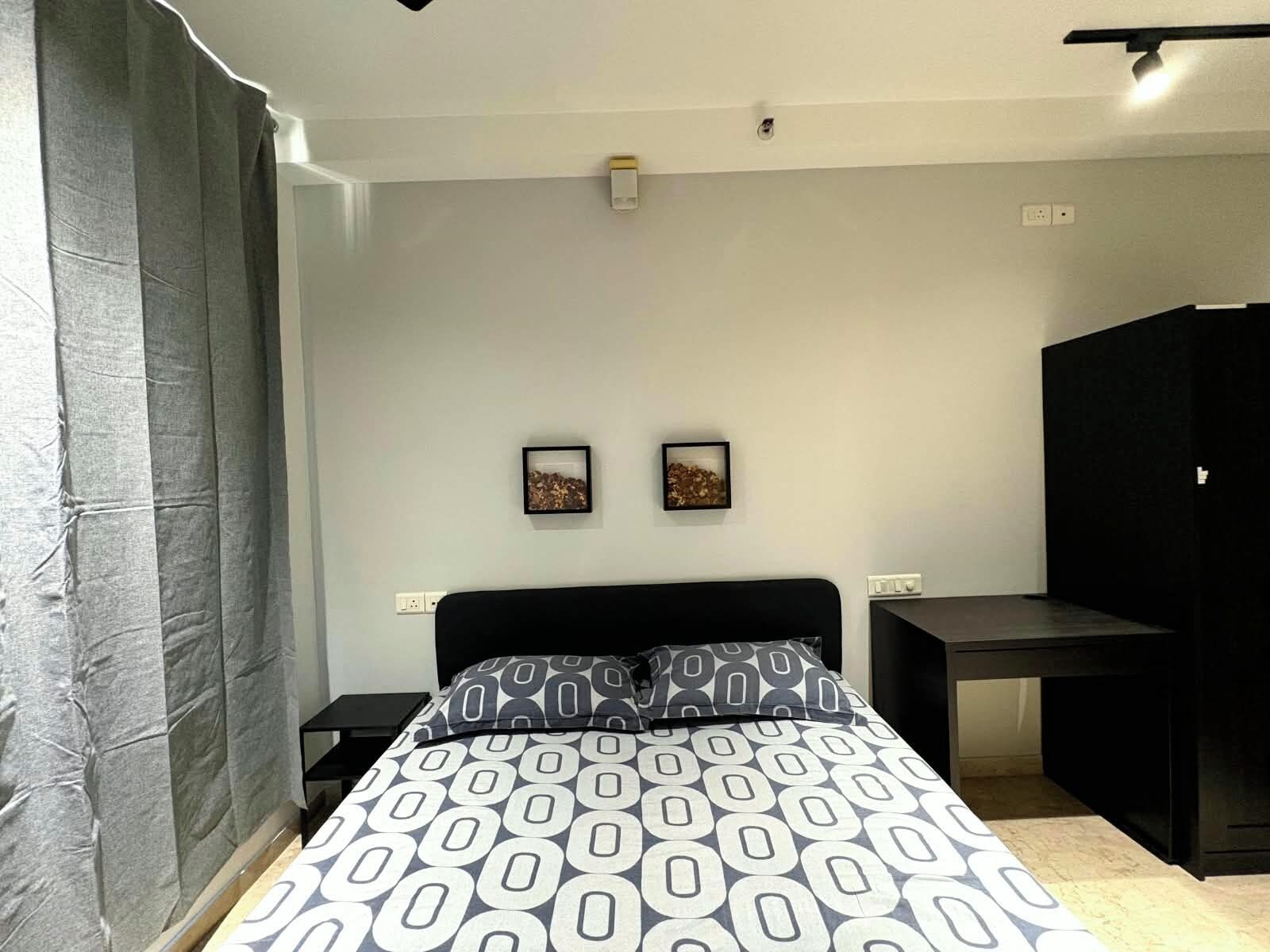 A bedroom with a bed, two bedside tables, a desk, and two framed pictures on the wall.