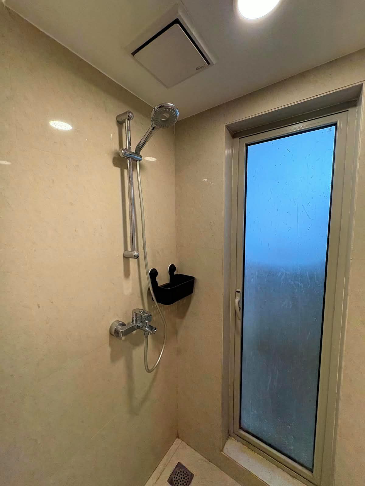 A bathroom with a shower, a window, and a small shelf.