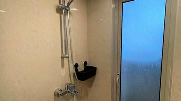 A bathroom with a shower, a window, and a small shelf.