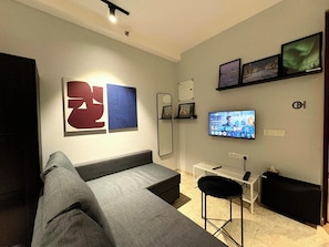 Een moderne woonkamer met een grijze bank, een aan de muur bevestigde televisie en abstracte kunstwerken.