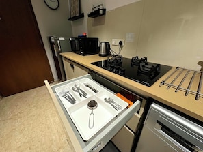 Een keuken met een ingebouwde kookplaat, een magnetron en een lade met keukengerei.