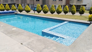 Ein rechteckiger Swimmingpool mit einer gefliesten Kante, umgeben von einer Betonplattform.