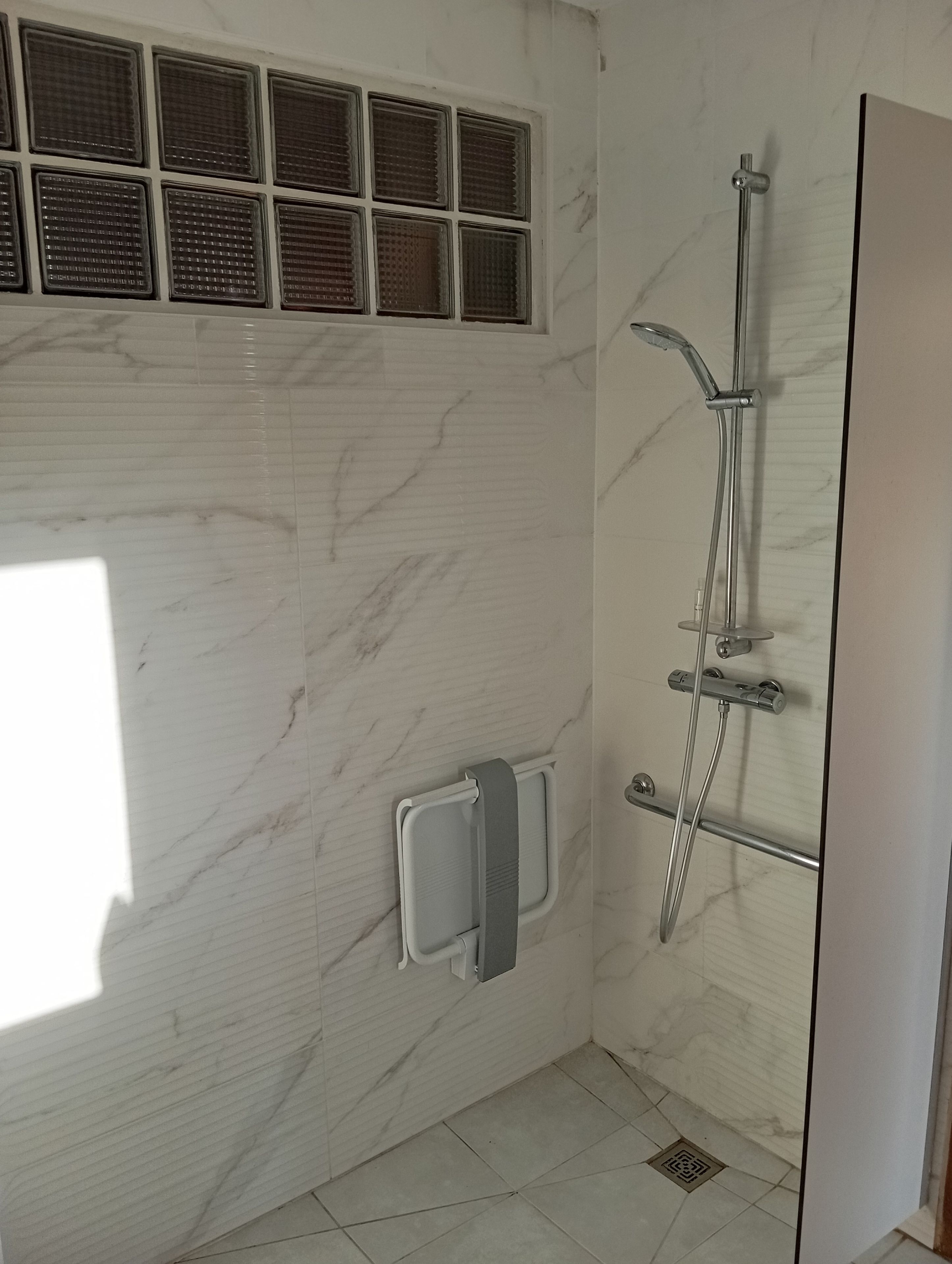 Een badkamer met een douche, een handdoekrek en een raam met zonwering.