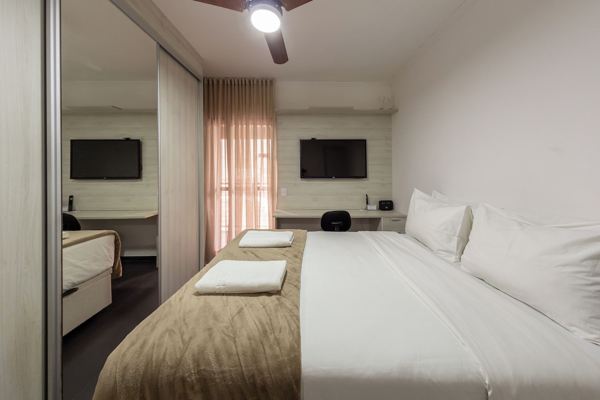 A hotel room with a bed, a desk, a chair, a TV, and a ceiling fan.