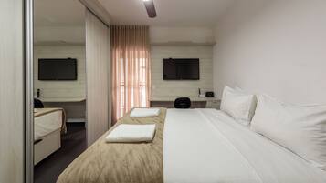 Una habitación de hotel con cama, escritorio, silla, televisor y ventilador de techo.