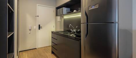 A compact kitchen with a stainless steel refrigerator, a microwave, and a built-in oven.