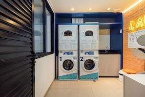 A laundry room with two front-loading washing machines, a sink, and a neon sign. - Moura by Bhomy (São Paulo)